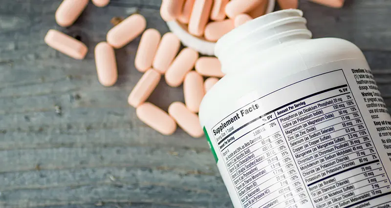 bottle of supplements laying on table with pills spilled out