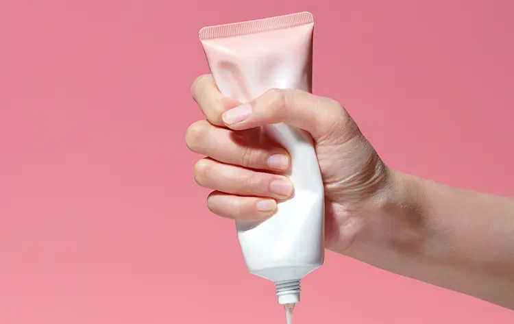 hand squeezing lotion tube with pink background